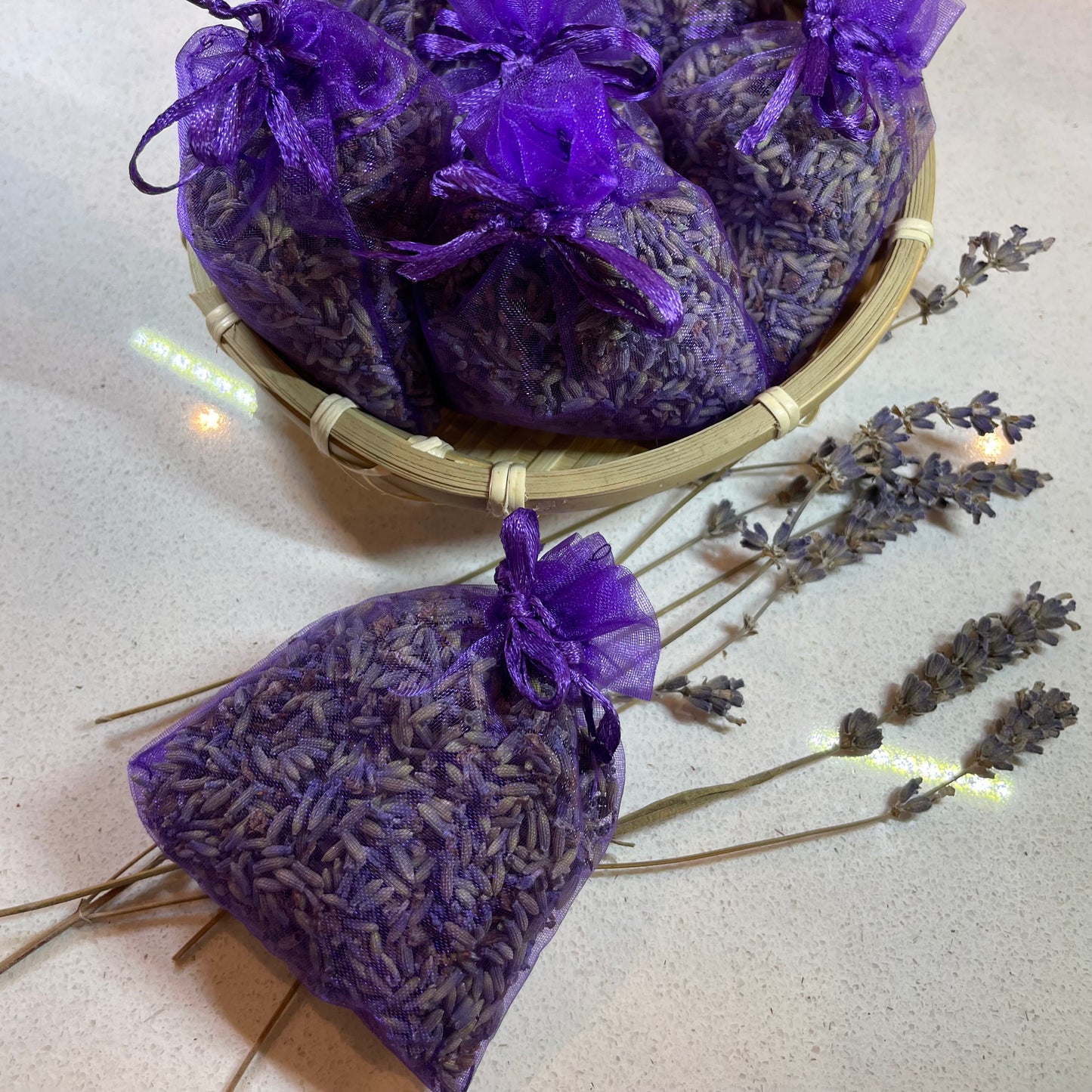 Purple lavender bags in a basket with dried lavender on a light surface