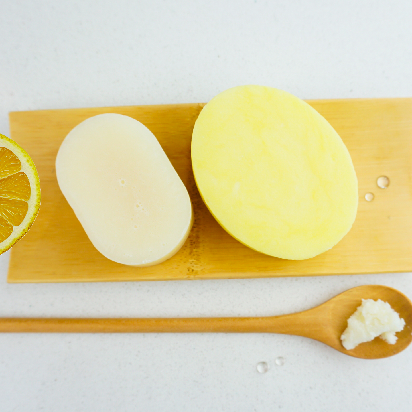Hydrating Lemon shampoo and condtioner bar surrounded by water droplets. Wooden spoon containing shea butter sits alongside the bamboo tray.
