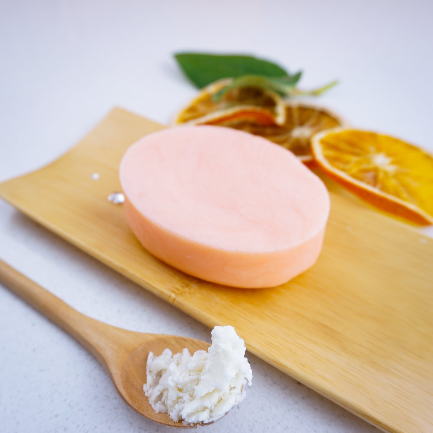 Orange Shampoo bar sitting on a bamboo tray beside a spoonful of shea butter