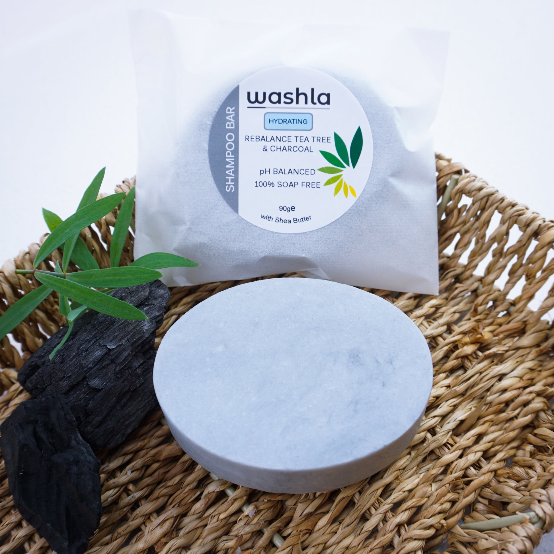 Washla Tea Tree and charcoal shampoo bar on hamper tray beside charcoal and some leaves