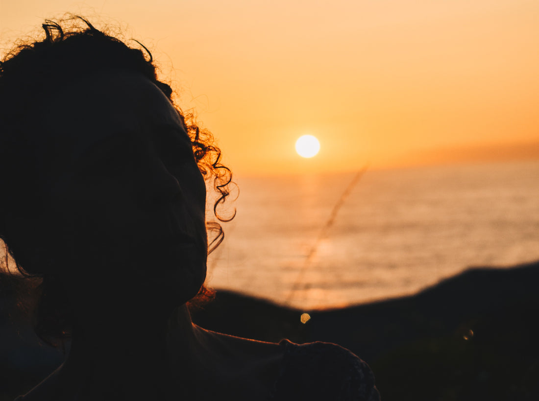 A woman with curly hair in the shadow of a sunset