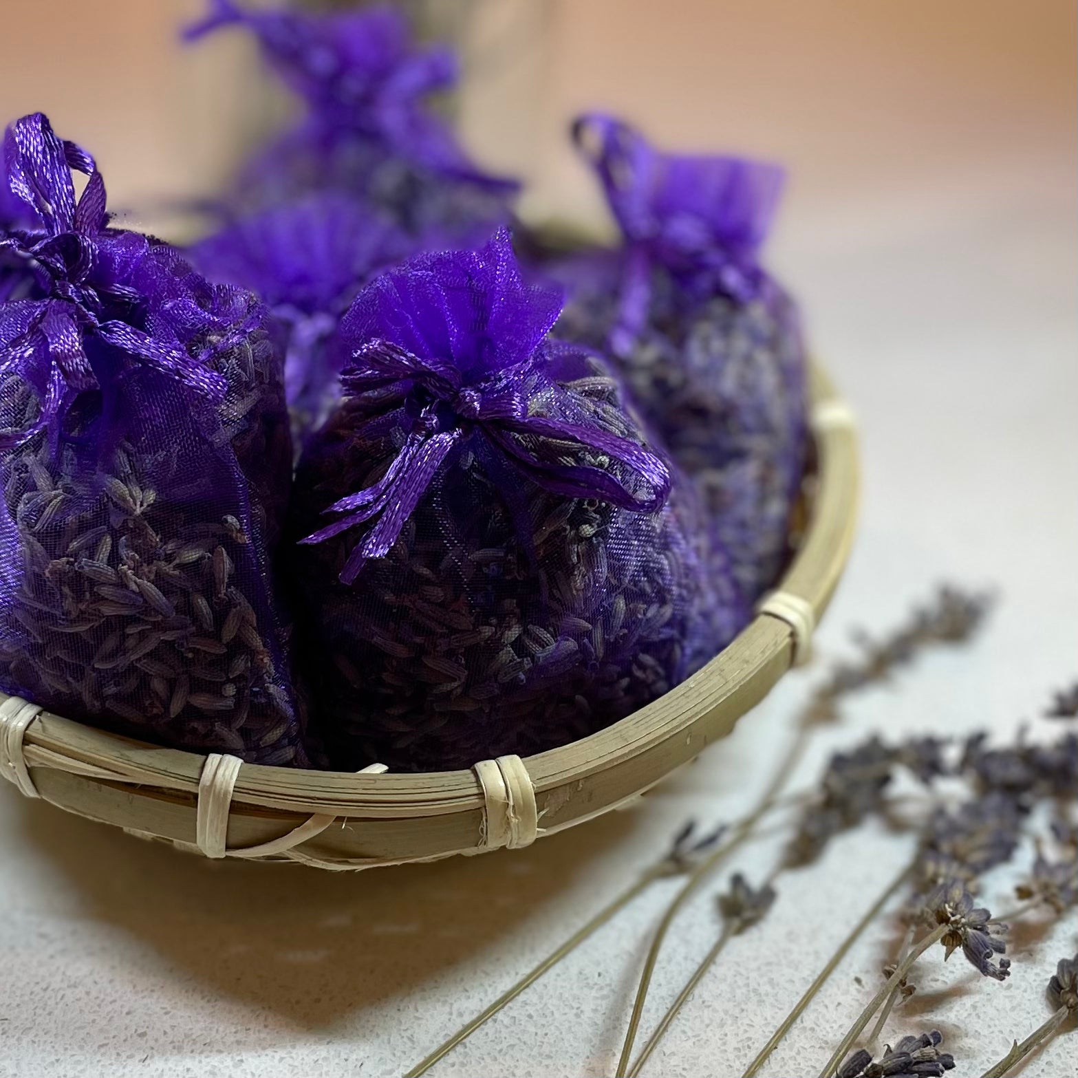 Purple lavender bags in a woven basket on a light surface with dried lavender.