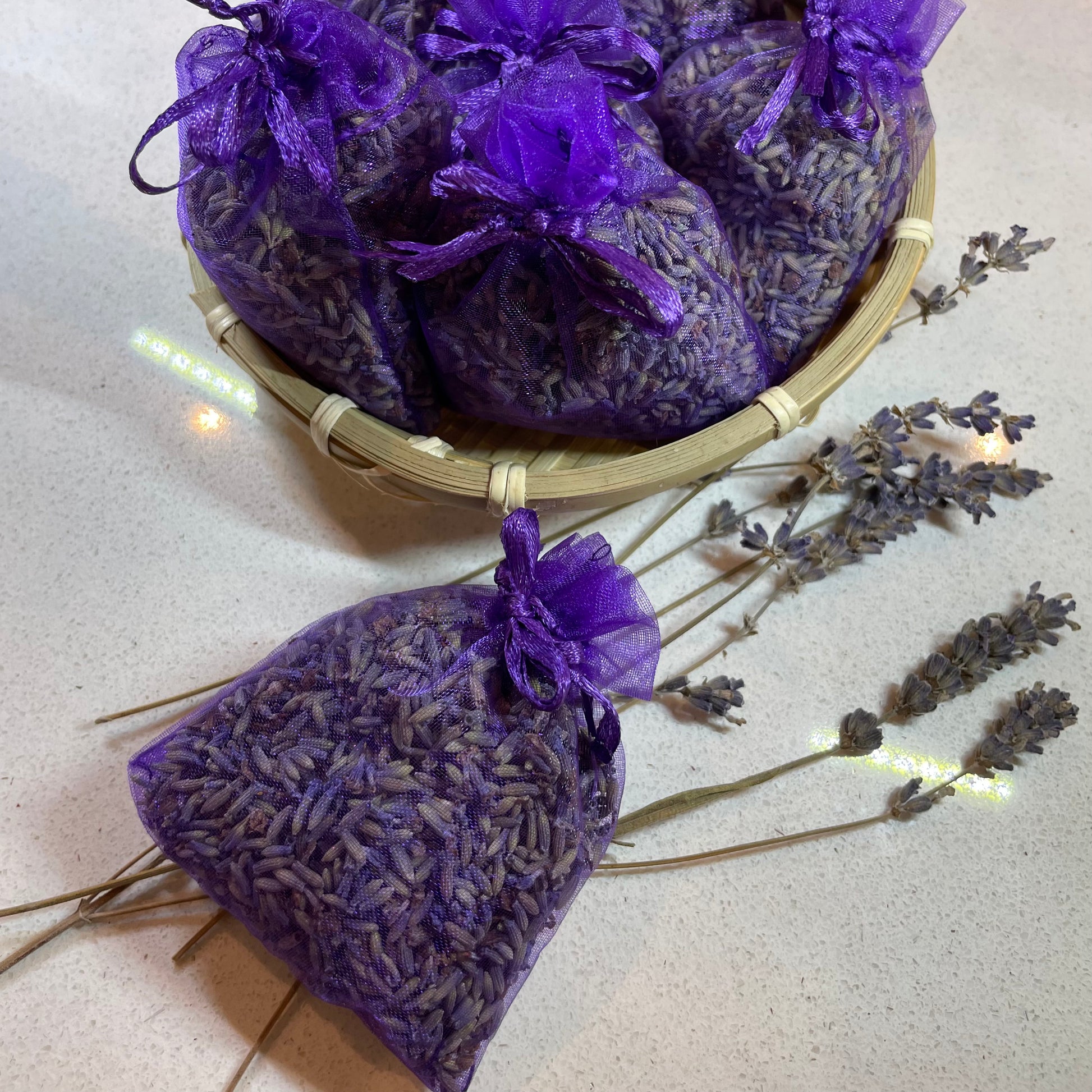 Purple lavender bags in a basket with dried lavender on a light surface