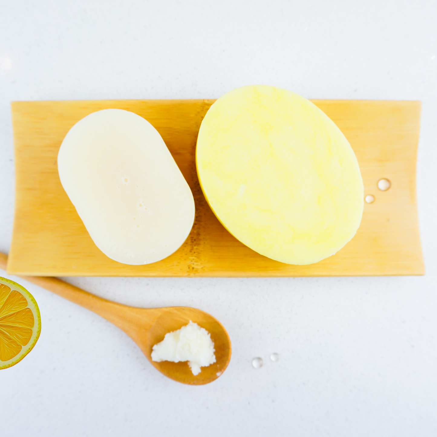 Lemon shampoo and conditioner bar sitting on bamboo tray with a slice of lemon