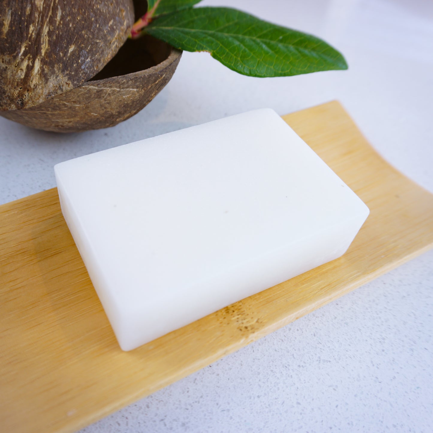 White coconut and almond soap bar on bamboo tray with coconut shell behind