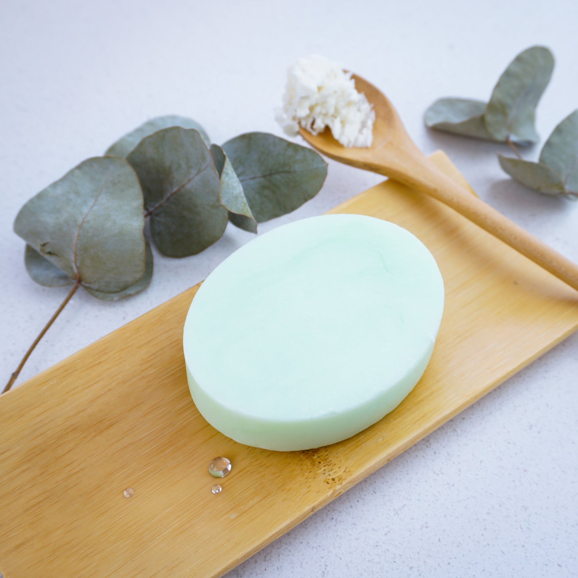 Washla Eucalyptus Shampoo Bar sitting on a bamboo tray surrounded by eucalyptus leaves