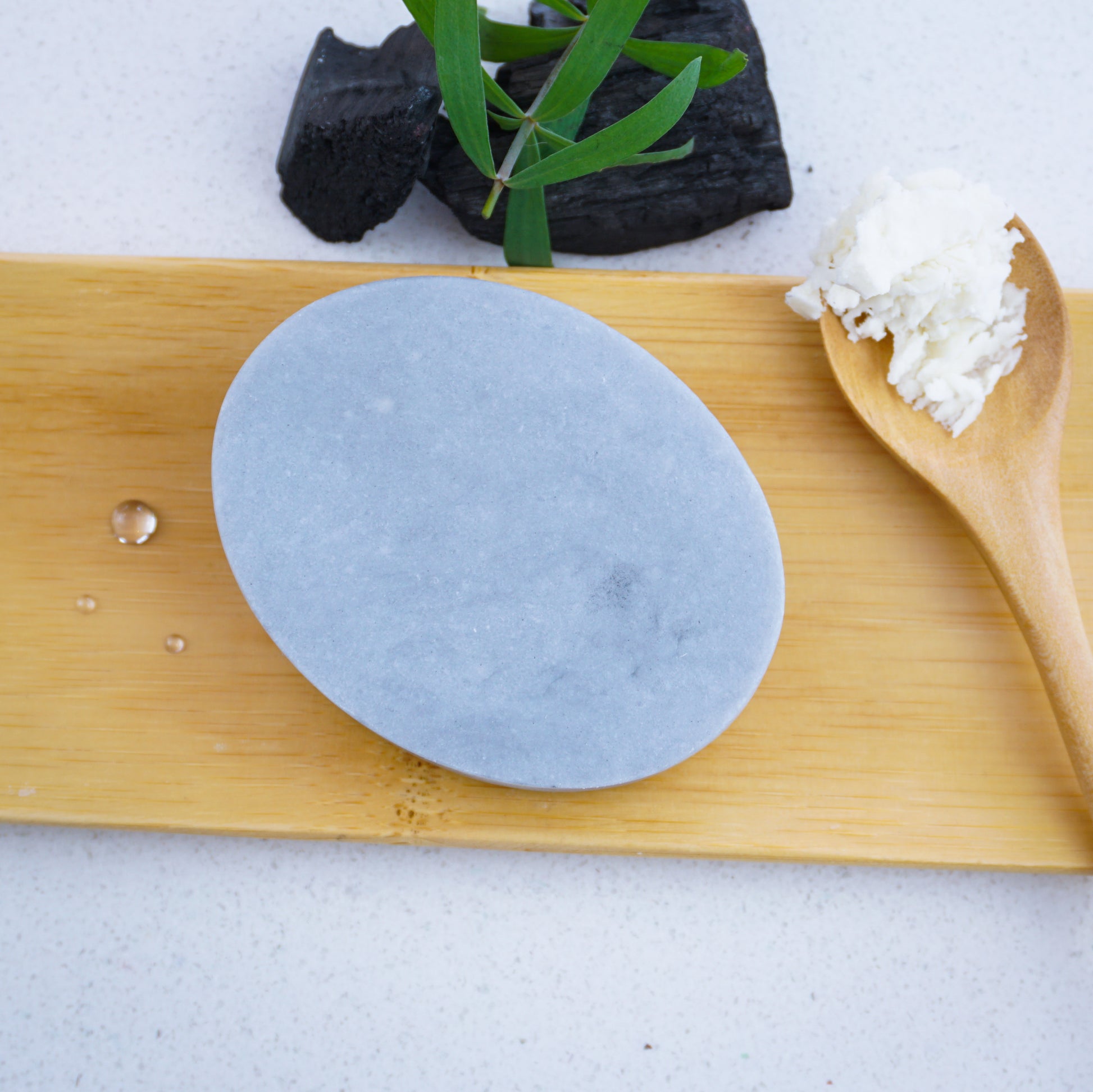Washla Tea Tree and Charcoal shampoo bar sitting on bamboo tray with a spoonful of shea butter