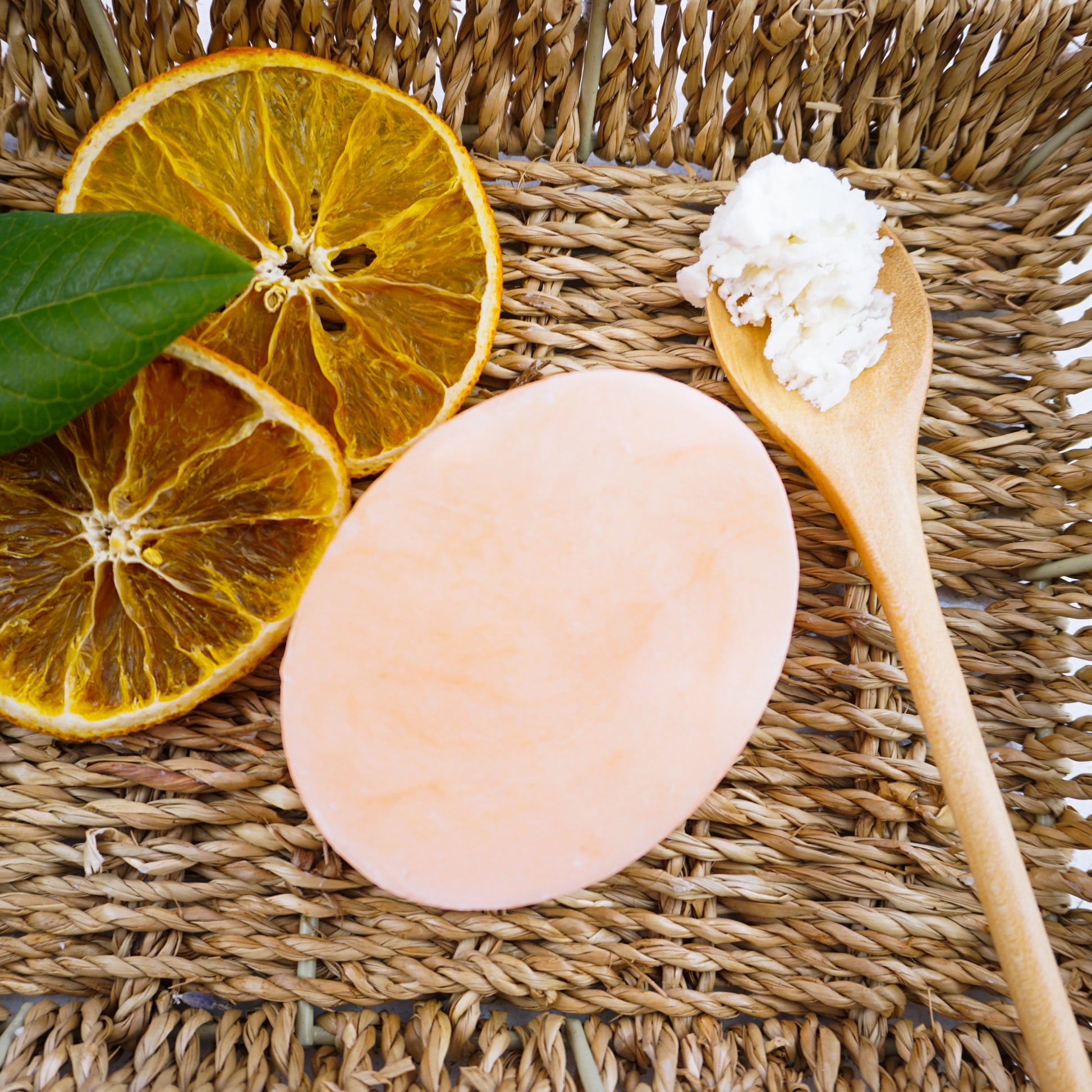 Sweet Orange Hydrating Shampoo Bar on hamper basket with two slices of dried oranges 