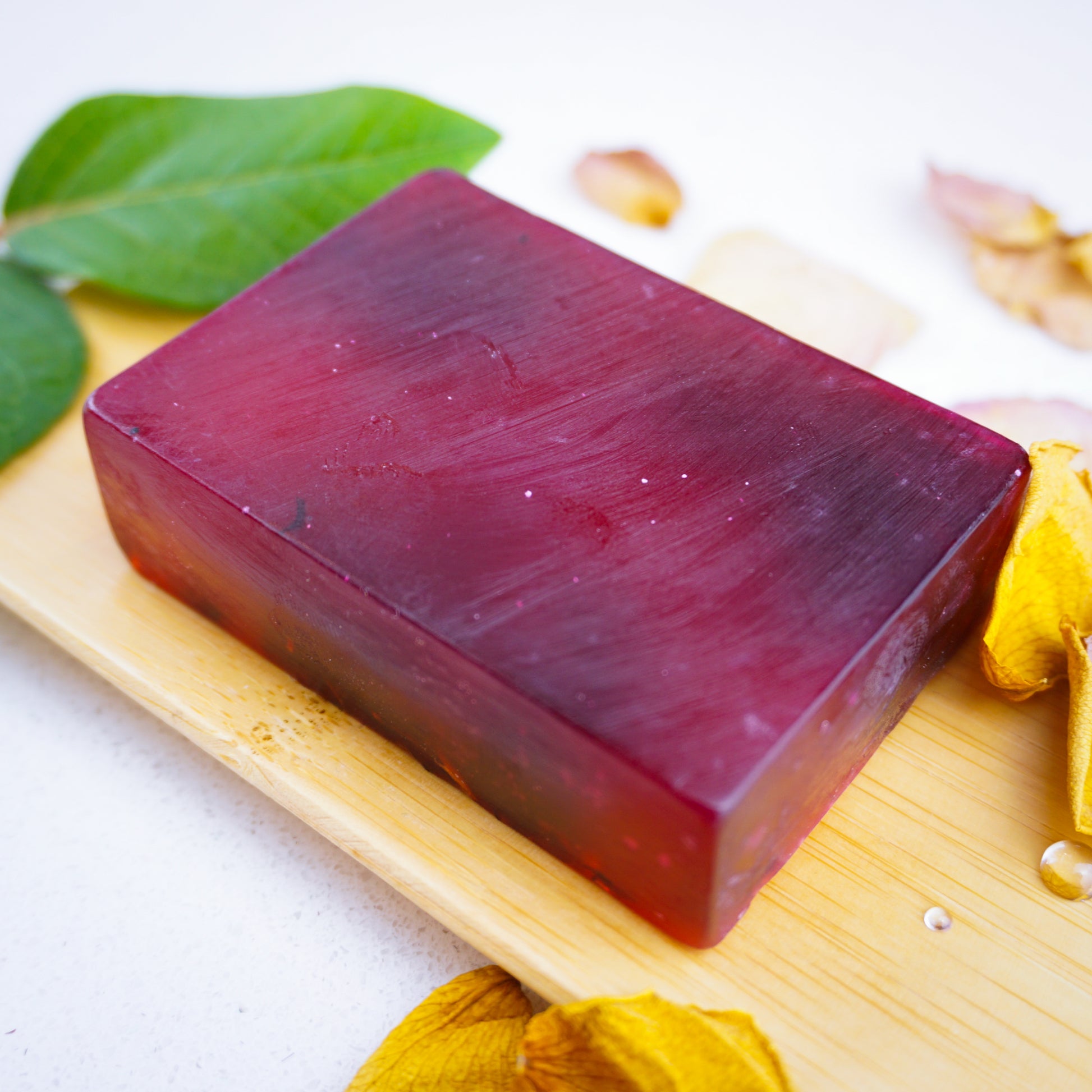 Rose & Ylang soap bar laid flat on bamboo tray with droplets and yellow rose petals